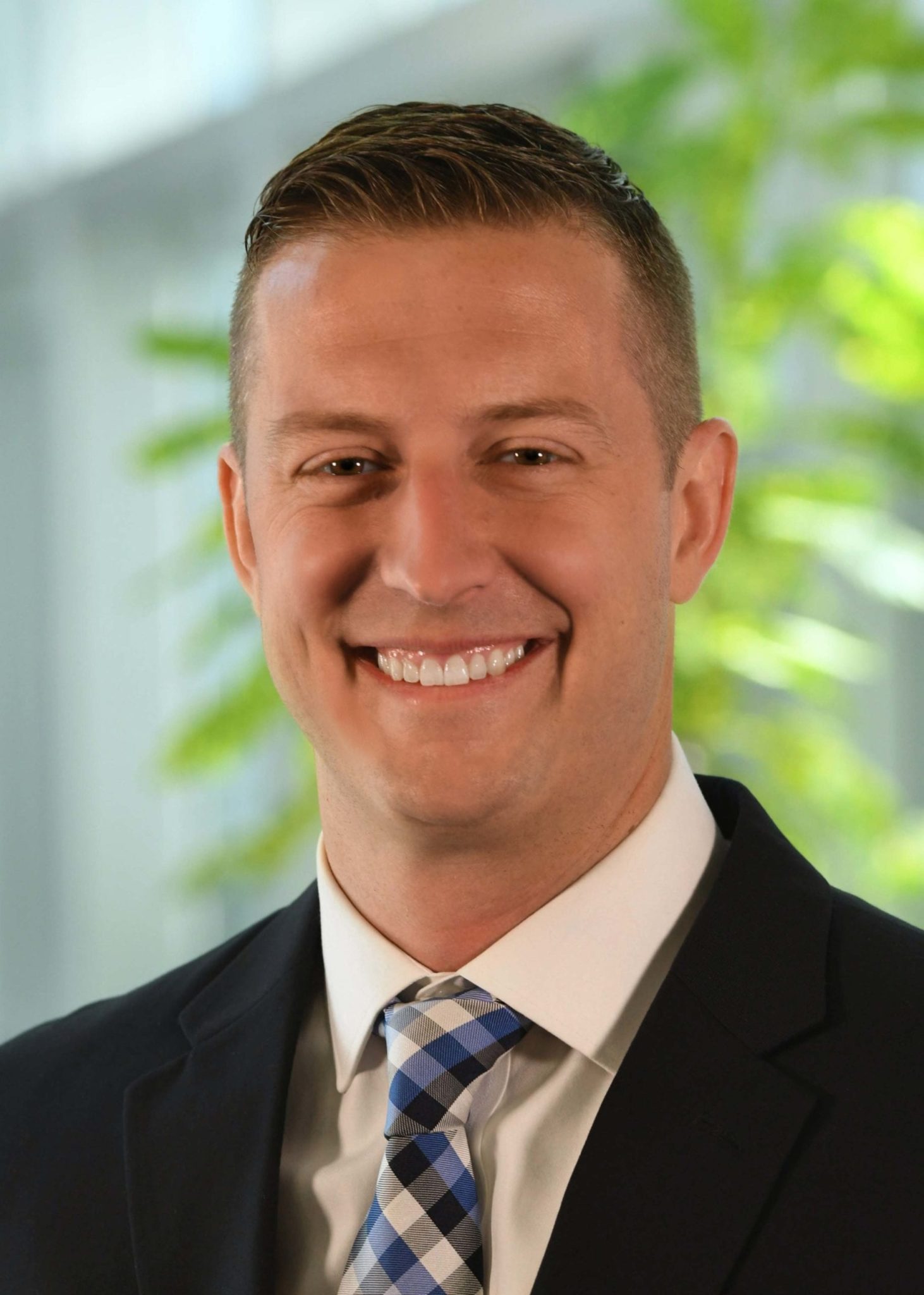 Prime's Recruiting Manager Travis Bacon, smiling while wearing a black suit with a blue & black tie.